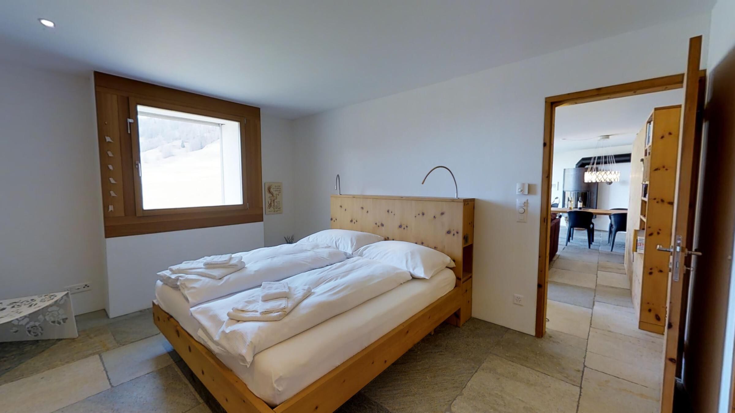 Una camera da letto con un letto di legno, una finestra e un ingresso verso una sala da pranzo.