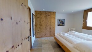 A bedroom with a wooden wardrobe, a bed with white linens, a painting of an eagle, and a window with natural light.