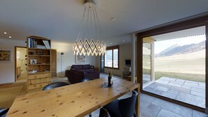 A modern living room with a wooden dining table, a purple sofa, and a large window offering a view of a mountainous landscape.