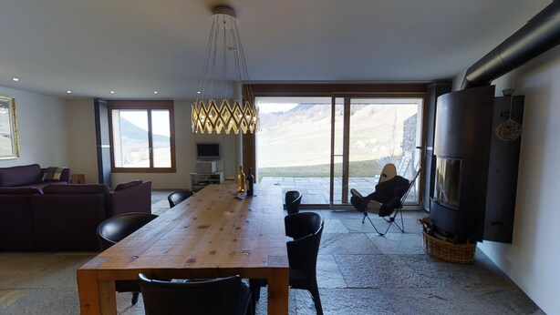 A modern living room with a wooden dining table, black chairs, a sofa, and a fireplace.
