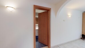 A hallway with a wooden door leading to a bathroom, white walls, and a tiled floor. - 2½-roomed apartment on the first floor, ca. (Silvaplana)