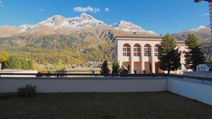 A building with arched windows and a flat roof, set against a backdrop of snow-capped mountains and a clear blue sky. - 2½-roomed apartment on the first floor, ca. (Silvaplana)