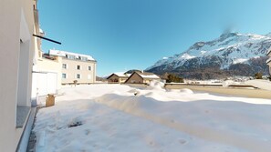 Rua coberta de neve com edifícios e uma montanha ao fundo.