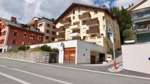 A multi-story hotel with balconies, a stone wall, and a clear sky. - 2½-roomed apartment on the first floor, ca. (Silvaplana)