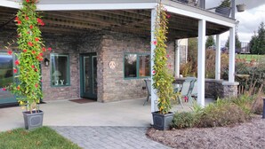 Un edificio con facciata in pietra, un patio coperto con posti a sedere all'aperto e piante in vaso con fiori rossi.