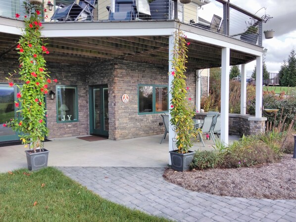 A building with a stone facade, a covered patio area with outdoor seating, and potted plants with red flowers. - Find out why this property is Almost Heaven (Swoope)