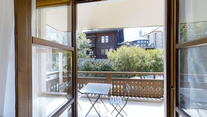A balcony with a table and chairs, a wooden fence, and a view of traditional buildings and trees. - Modern 2½-room apartment in the first floor, about 60m2. (Maloja)