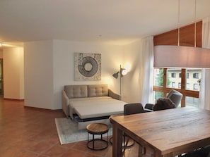 A modern living room with a sofa, a dining table, and a lamp.