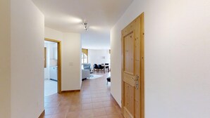 A hallway with a wooden door, a dining area with a table and chairs, and a kitchen visible through an open door. - Modern 2½-room apartment in the first floor, about 60m2. (Maloja)