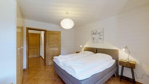 A bedroom with a bed, bedside lamps, a wall art piece, and a door leading to another room. - Modern 2½-room apartment in the first floor, about 60m2. (Maloja)