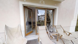 Eine Terrasse mit Tisch und Stühlen, eine Glastür zum Raum hin und Blick auf eine Wohngegend.