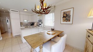 Une cuisine moderne avec des meubles blancs, une table à manger en bois et un lustre original en forme de bois de cerf.