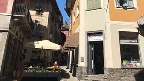 Rua com edifícios, mesas ao ar livre e uma loja com letreiro.