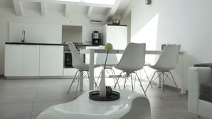 Cozinha moderna com armários brancos, área de refeições com mesa e cadeiras brancas e um claraboia acima.