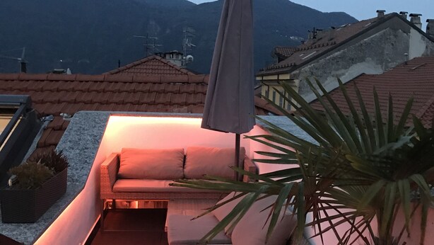 Terraço no telhado com área de estar acolchoada, planta em vaso e vista para montanhas distantes.