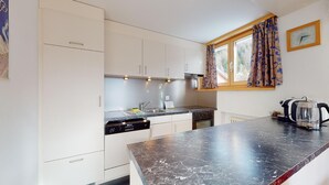 Ett modernt kök med vita skåp, en svart bänkskiva i marmor, en inbyggd ugn och ett fönster med mönstrade gardiner.