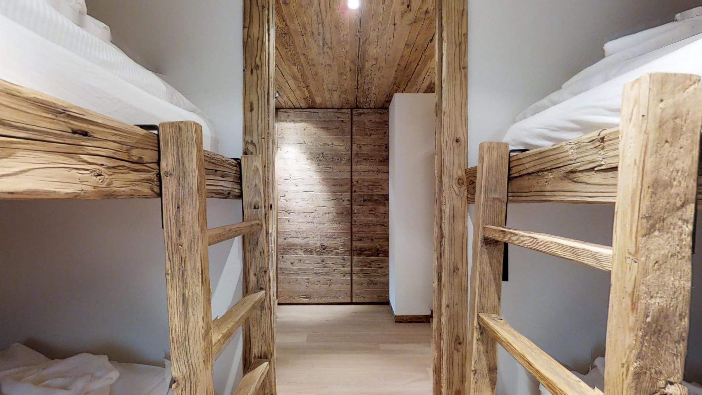A narrow wooden corridor leading to a room with bunk beds and a wooden ceiling.