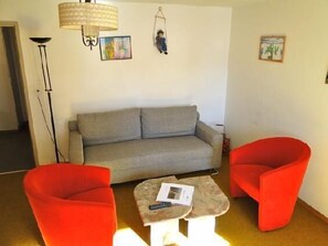 A living room with a grey sofa, two red armchairs, a small coffee table, a floor lamp, and wall art.