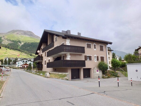 A multi-story hotel with balconies, a parking area, and a mountainous backdrop.