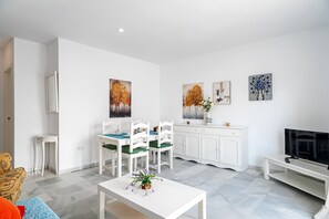 Un salon moderne comprenant un coin repas, des meubles blancs, un téléviseur à écran plat et des œuvres d’art accrochées aux murs.
