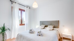 A neatly made bed with rolled towels, a bedside table with a lamp, and a potted plant. - Casa Delicias pool near the beach in Alcudia (Alcúdia)