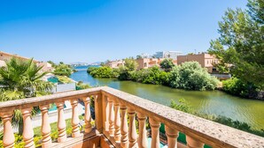 A balcony with a view of a river, greenery, and buildings in the background. - Casa Delicias pool near the beach in Alcudia (Alcúdia)