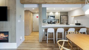 A modern kitchen with a central island, white bar stools, a wooden dining table, and a TV mounted on the wall.