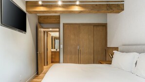 A bedroom with a bed, wooden wardrobe, and a television mounted on the wall.