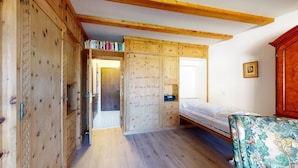 A room with a wooden wardrobe, a bed with a floral bedspread, and a wooden cabinet with books.