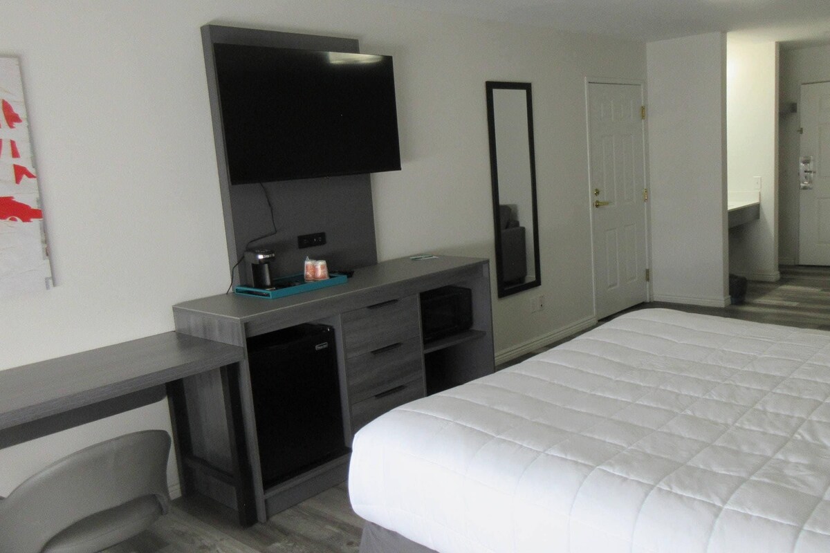 A hotel room with a bed, a desk with a television, a mirror, and a chair.