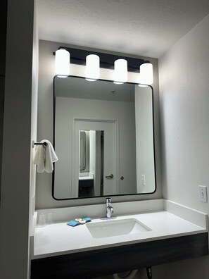A bathroom with a white sink, a mirror with lights, and a towel rack.