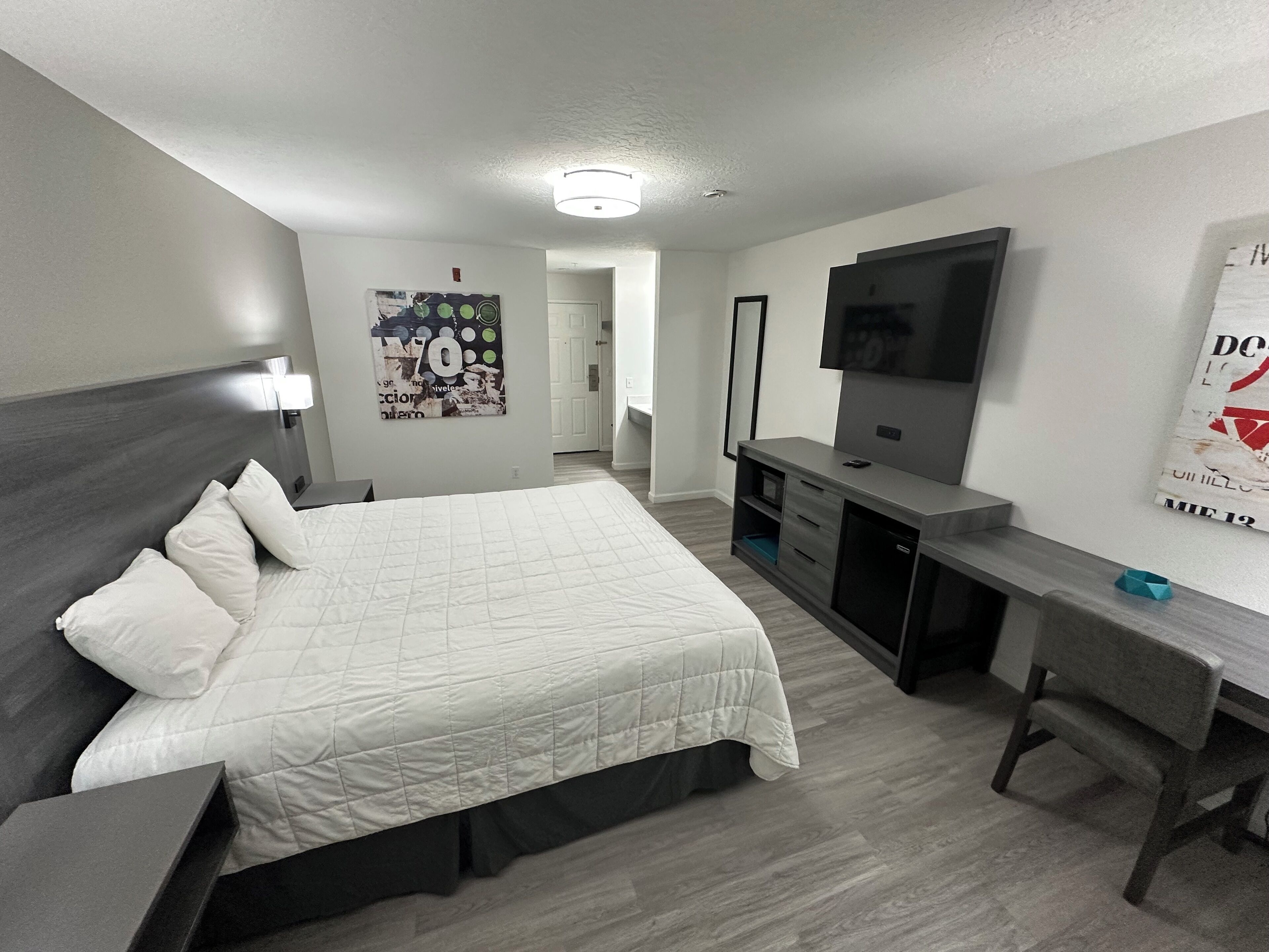 A modern hotel room with a bed, desk, TV, and a door leading to another room.