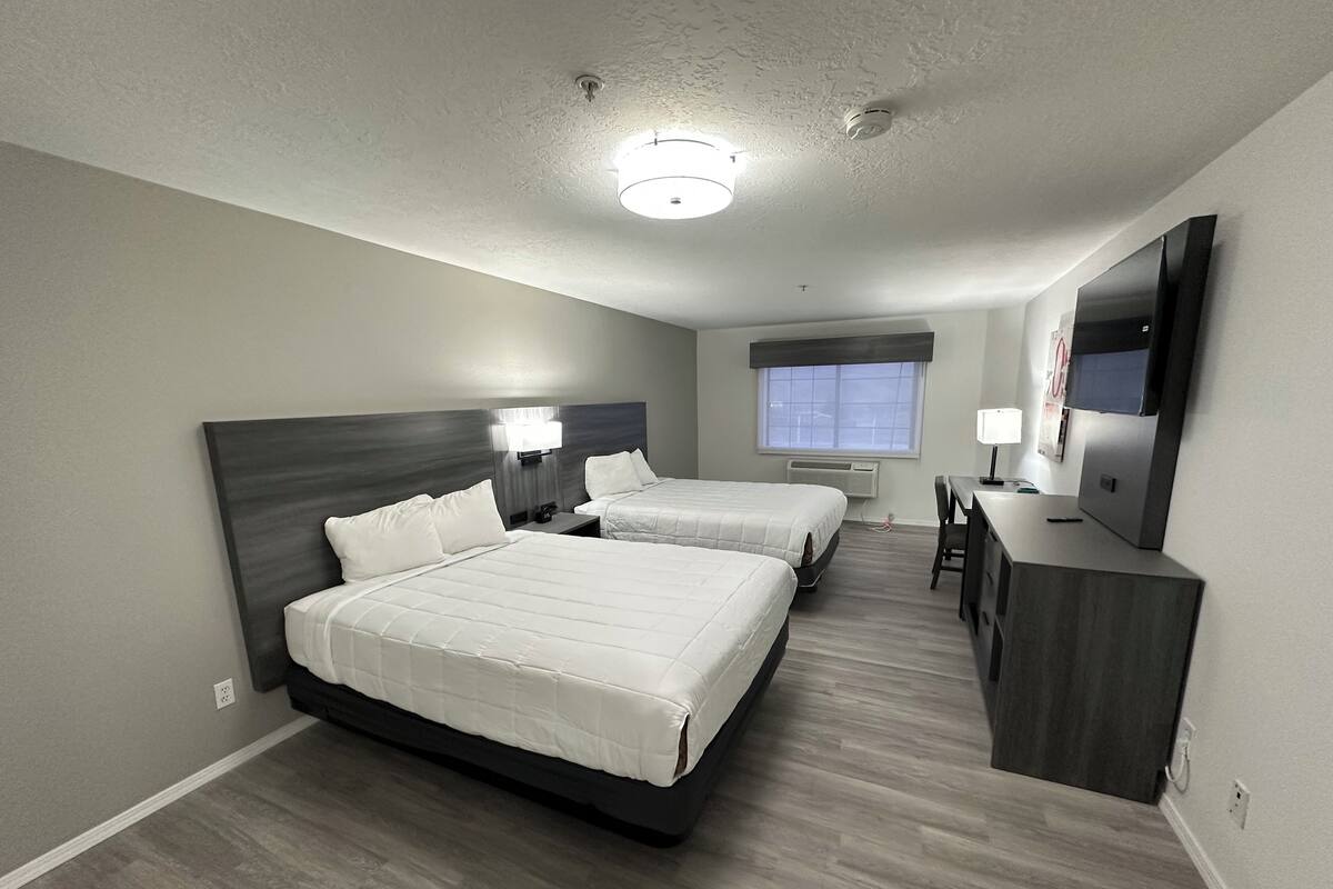 A hotel room with two beds, a desk, a chair, a TV, and a window.