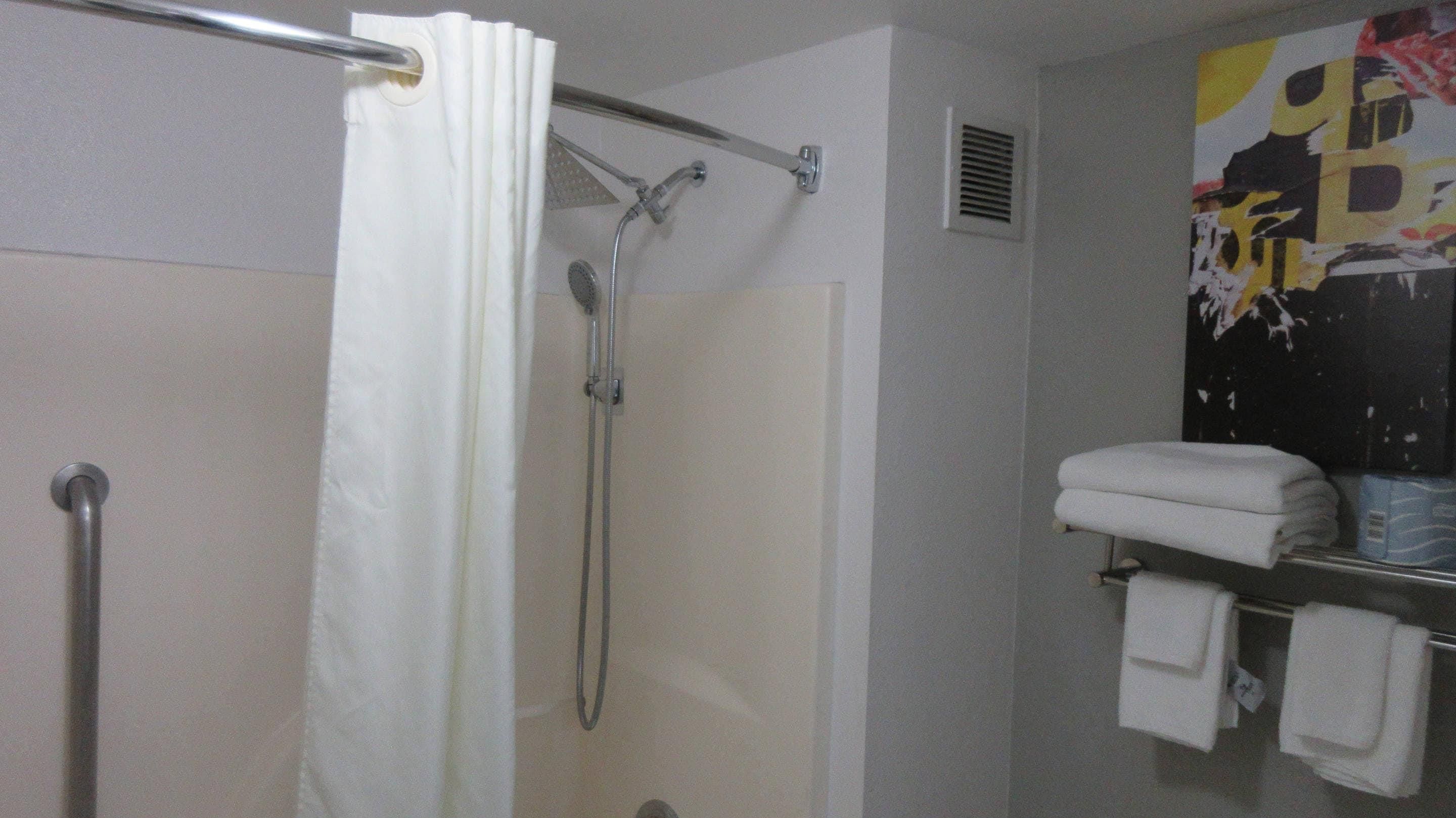 A shower with a white curtain, a handheld showerhead, and a towel rack with folded towels.