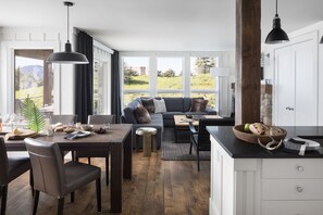 A modern kitchen with a dining area, large windows, and a view of the outdoors.