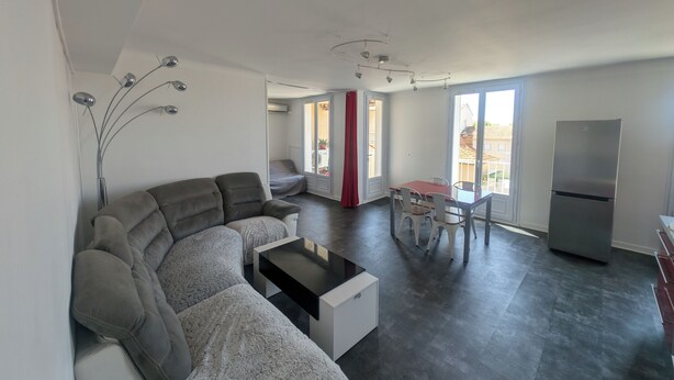 A modern living room with a grey sectional sofa, a coffee table, and a dining area with a table and chairs. There is a large window providing natural light and a view of the outside. - 58m2 flat in ST Raphael-600 metres from the beach and train station-free parking (Saint-Raphaël)