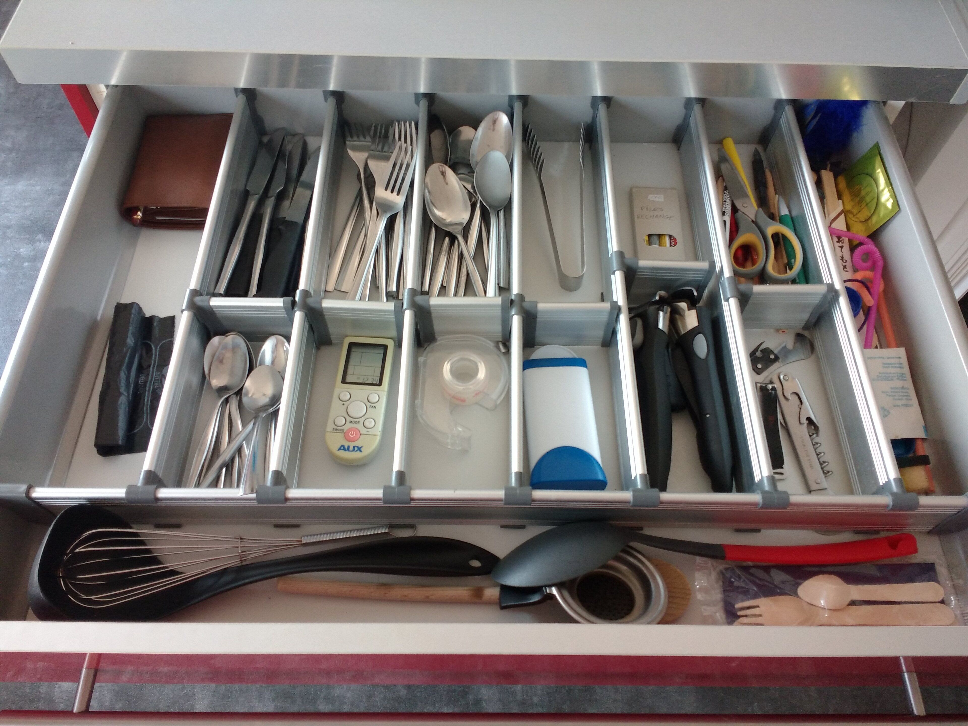 A kitchen drawer with utensils, a digital scale, and a whisk.