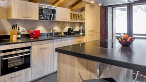 Une cuisine moderne avec des meubles en bois, un four encastré et un grand îlot central doté d’un plan de travail noir.