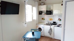 A compact kitchen with a washing machine, microwave, and sink. There's a table with chairs and a clock on the wall. - DISCOVER MY CHARMING BUNGALOW WITH POOL (Le Gosier)