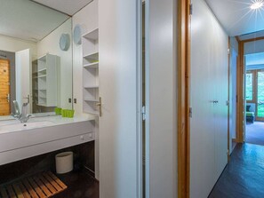 Un bagno con lavandino, specchio e mensole. Si apre una porta verso un'altra stanza.