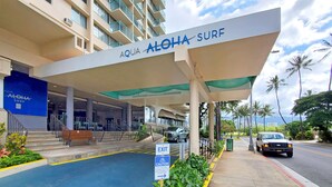 L’entrée d’Aqua Aloha Surf se distingue par une allée couverte, un escalier et une vue sur la rue, bordée de palmiers.