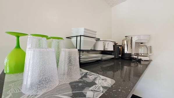 A kitchen counter with a coffee maker, a kettle, and a stack of white plates. - Affordable, Central Steps to the Beach & Canal (Honolulu)