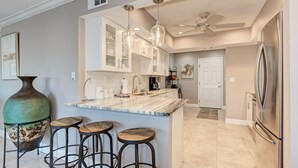 A kitchen with a marble island, bar stools, stainless steel appliances, and pendant lighting. - Spacious beachfront Penthouse 3 bed/3 bath suite, Stunning Gulf views! (Siesta Key)