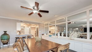 A spacious dining area with a wooden table and chairs, a ceiling fan, and a view into the kitchen and living areas. - Spacious beachfront Penthouse 3 bed/3 bath suite, Stunning Gulf views! (Siesta Key)