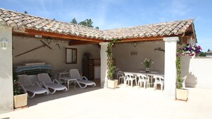 A covered outdoor area with lounge chairs, a table, and potted plants.