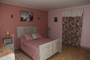 A bedroom with a bed, a nightstand, a lamp, a painting on the wall, and a floral curtain. - Rental Magnificent Provencal farmhouse of espiguette in a regional park Alpille (Saint-Rémy-De-Provence)
