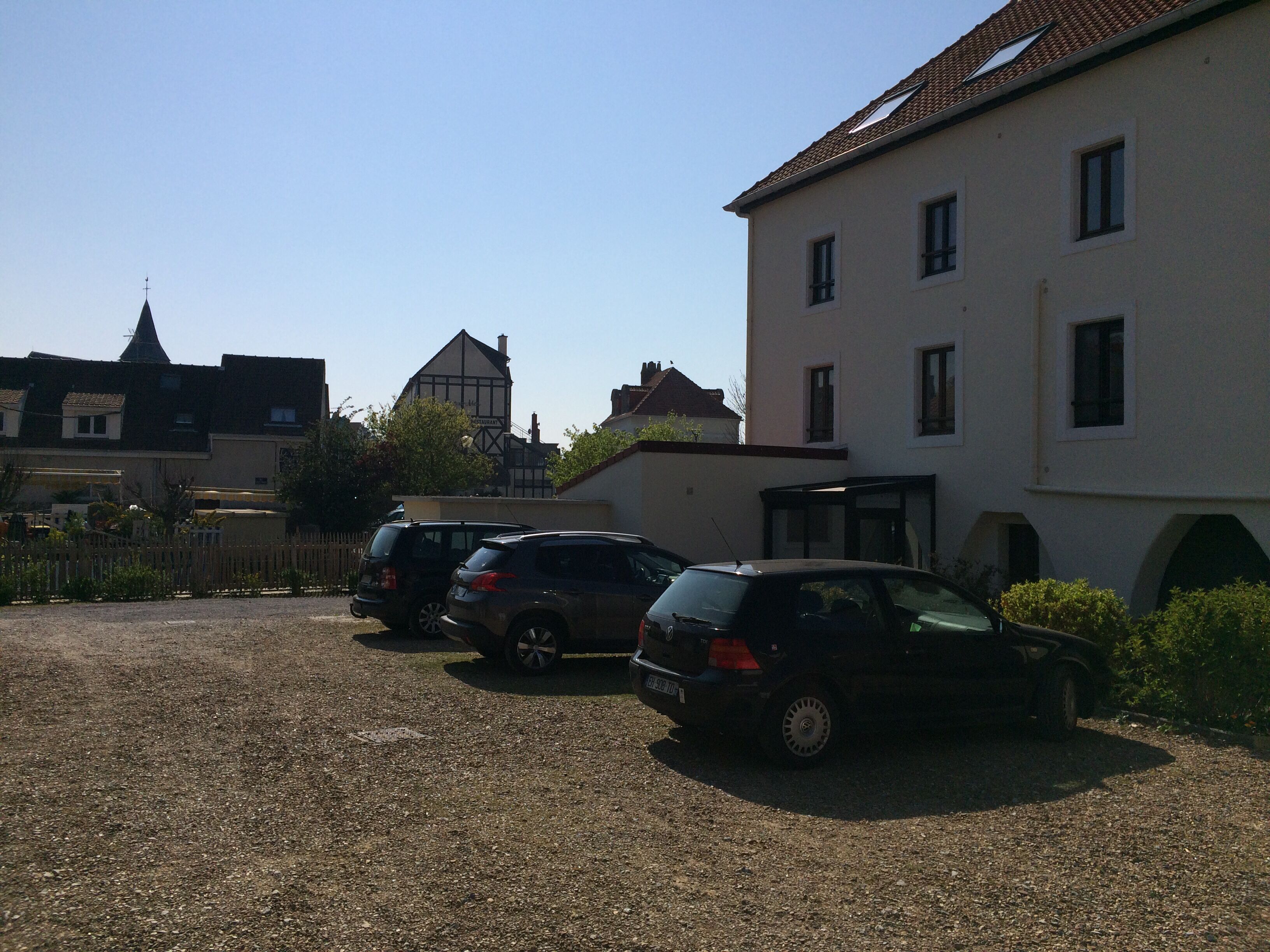 A parking area with several cars parked in front of a building with multiple windows and a sloped roof.