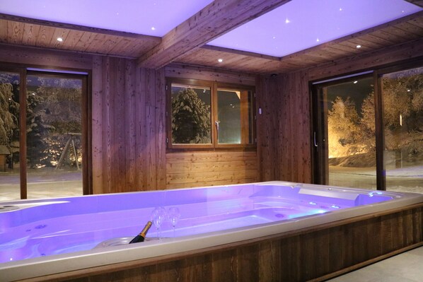 Een houten vakantiehuis met een hottub, grote ramen en uitzicht op bomen.