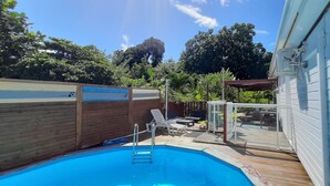 A backyard with a swimming pool, wooden deck, and a covered patio area. - Villa Familiale 8p Piscine Sécurisée & Jardin PMR (Le Gosier)