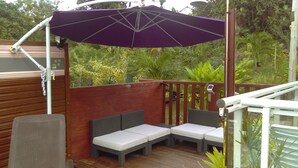 A covered outdoor seating area with a purple umbrella, wooden deck, and surrounding greenery. - Villa Familiale 8p Piscine Sécurisée & Jardin PMR (Le Gosier)